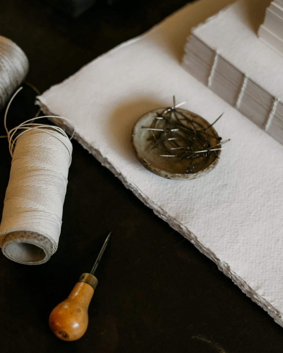 Two spools of thread, a needle, and a pin cushion on a dark surface.