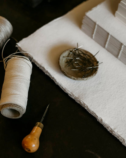 Two spools of thread, a needle, and a pin cushion on a dark surface.