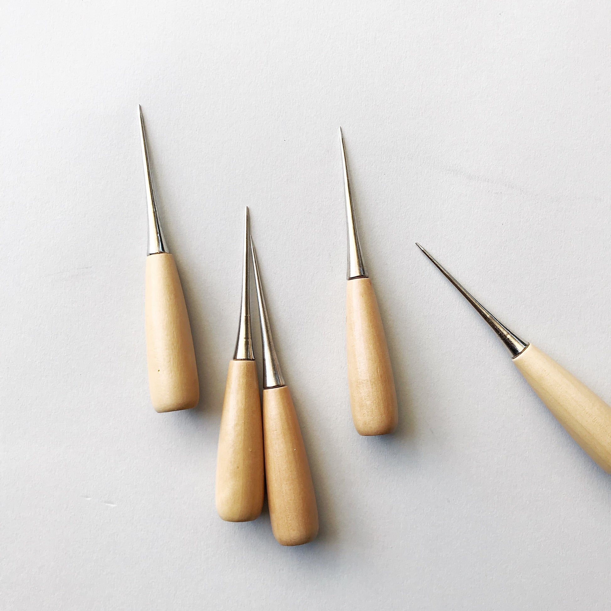 Set of four wooden-handled tools with metal tips on a light gray background