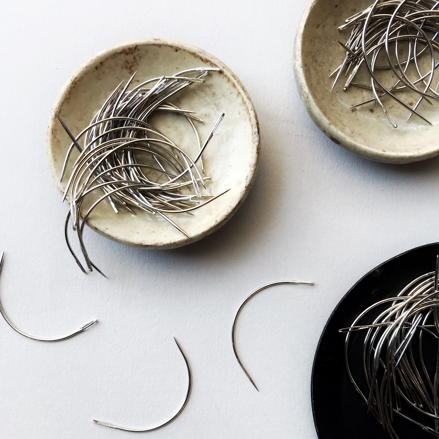 Three ceramic plates with bookbinding needles on a light gray background