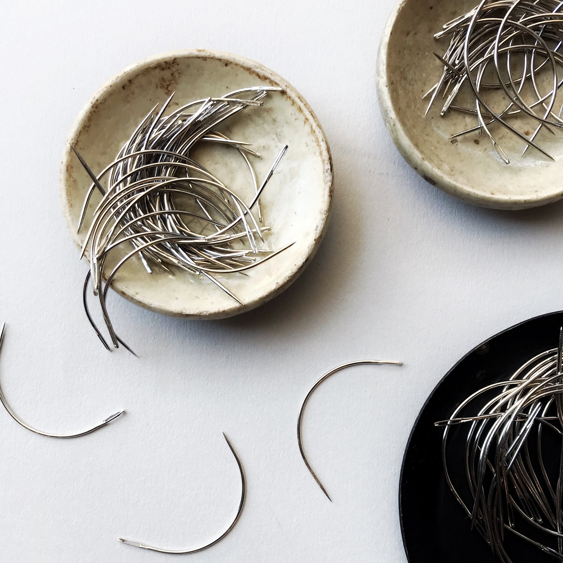 Three ceramic plates with bookbinding needles on a light gray background