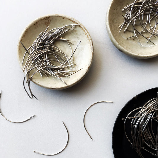 Three ceramic plates with bookbinding needles on a light gray background